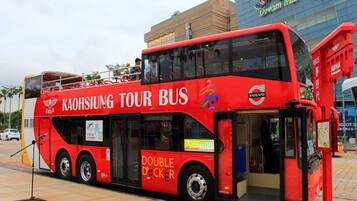 Un autobús turístico rojo de dos pisos con la inscripción "Kaohsiung Tour Bus" y "Doble Piso", estacionado frente a un edificio con el letrero "Dream Mall".