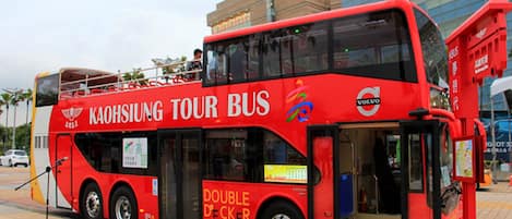 Un autobús turístico rojo de dos pisos con la inscripción "Kaohsiung Tour Bus" y "Doble Piso", estacionado frente a un edificio con el letrero "Dream Mall".