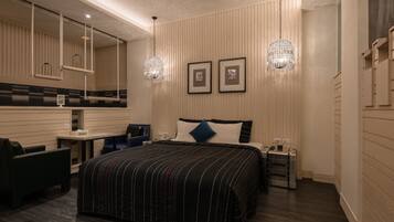 Habitación de hotel moderna con una cama grande, un escritorio y una silla. Hay dos luces empotradas en la pared y cuadros enmarcados sobre la cama.
