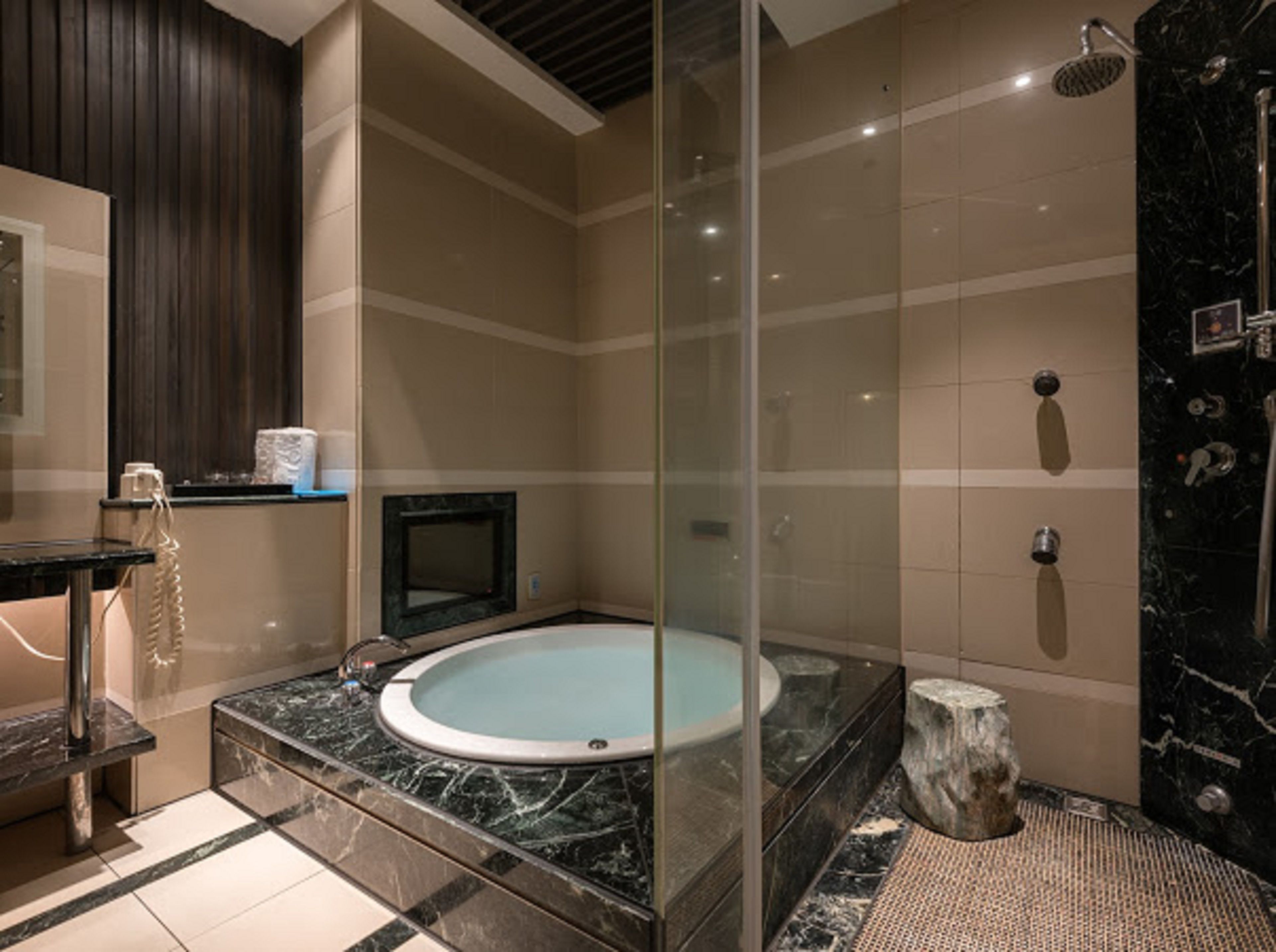 A modern bathroom with a glass-enclosed jacuzzi, a vanity with a mirror, and a shower area with a marble wall.