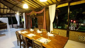 A dining area with a long wooden table set for a meal, surrounded by chairs. - Kubu Ampo Villa (Kerobokan)