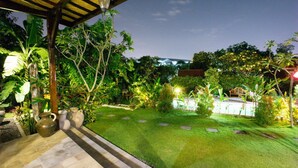A well-maintained garden with a thatched roof structure, stone pathway, and various plants. - Kubu Ampo Villa (Kerobokan)
