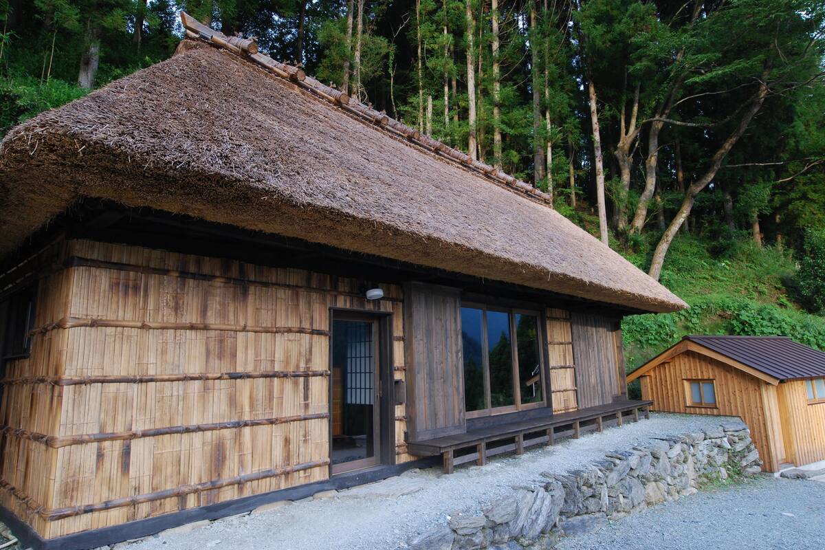 Une maison traditionnelle en bois, avec un toit de chaume, de grandes fenêtres et des fondations en pierre.