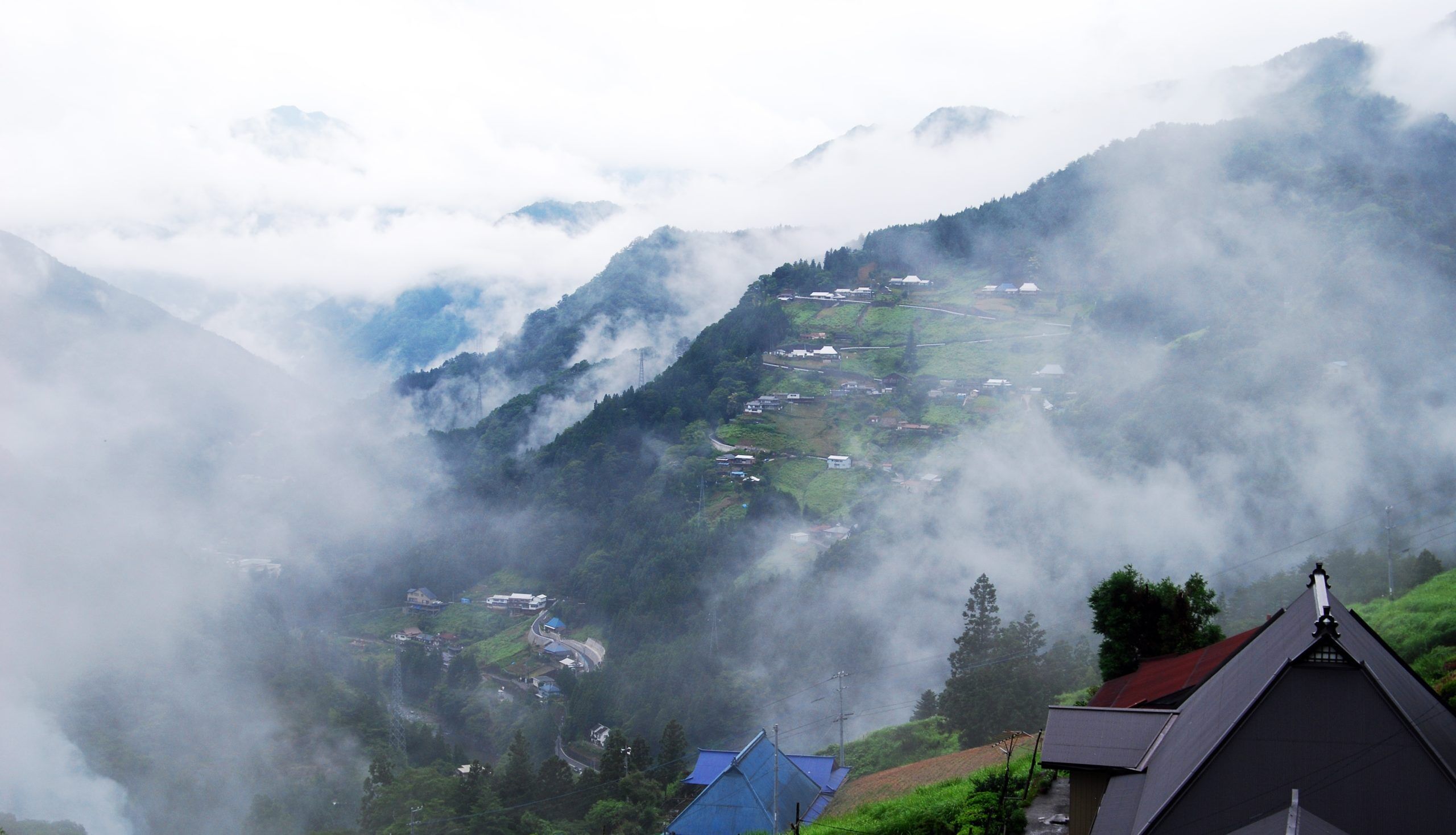A mountainous village with houses nestled among the hills, surrounded by dense fog.