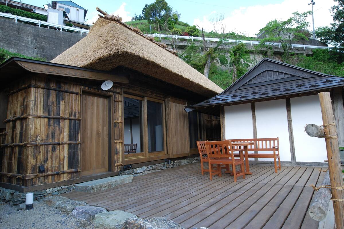 Un bâtiment traditionnel en bois, doté d’un toit de chaume, d’une terrasse en bois et d’un banc.
