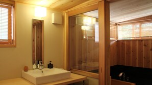 Ein Badezimmer einer Holzhütte mit einem großen Spiegel, einem weißen Waschbecken und einem Fenster mit Jalousien.