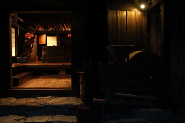 A dimly lit wooden interior with a stone floor, a wooden staircase, and a small seating area.