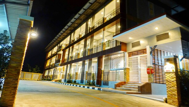 Un hotel de varios pisos con balcones, una entrada bien iluminada y un camino de acceso con portón.