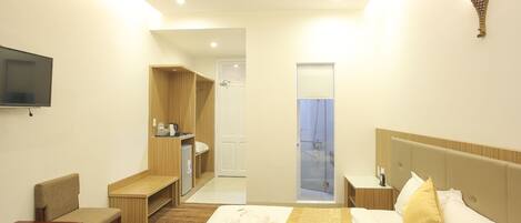 Habitación de hotel con cama, zona de estar, televisor, ducha y kitchenette pequeña.