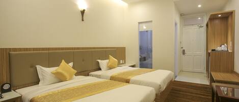 A hotel room with two beds, a desk, a chair, a nightstand, and a wall-mounted lamp.
