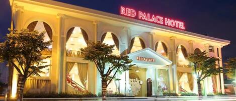 Exterior del Hotel Palacio Rojo, con arquitectura neoclásica, ventanas arqueadas y señalización iluminada.