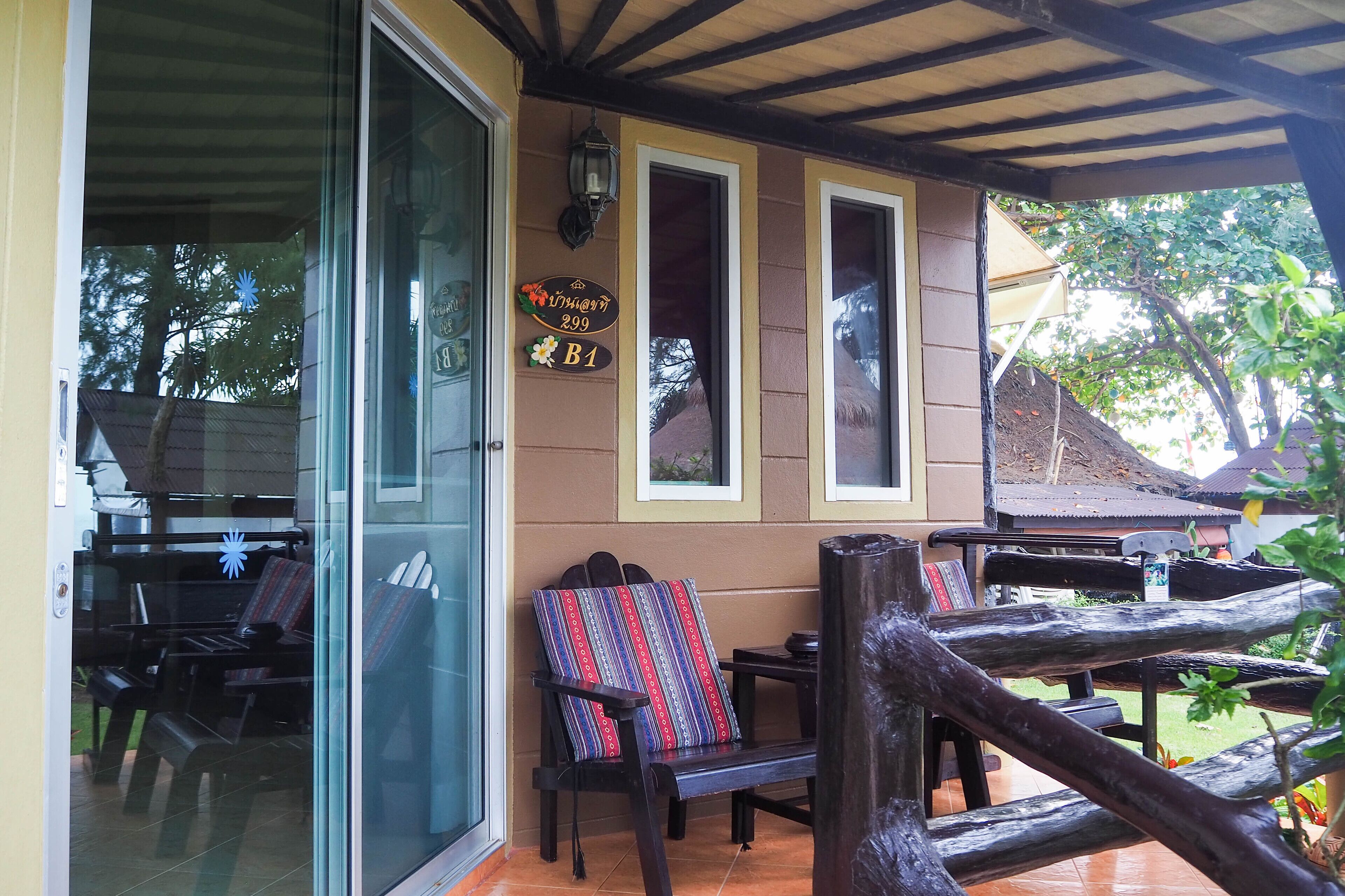 A covered outdoor seating area with wooden furniture and a glass door leading inside.