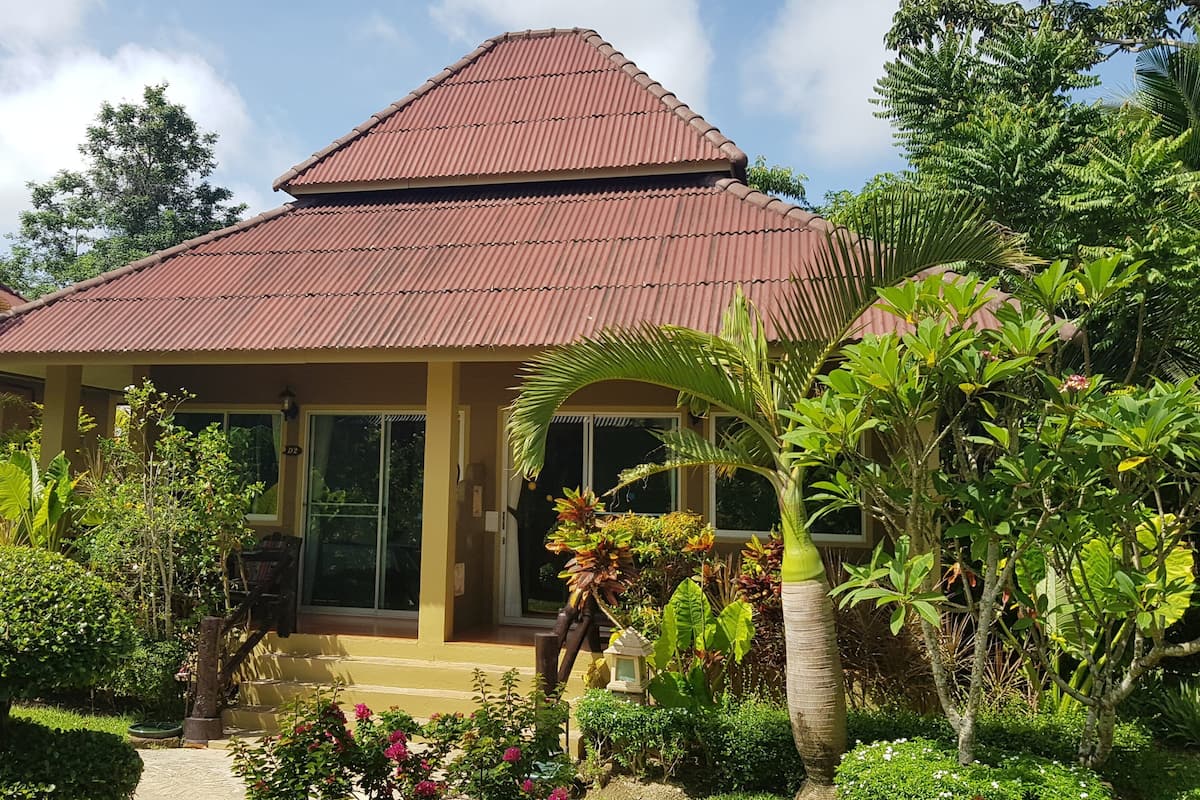 A two-story house with a red roof, surrounded by lush greenery and a well-maintained garden.