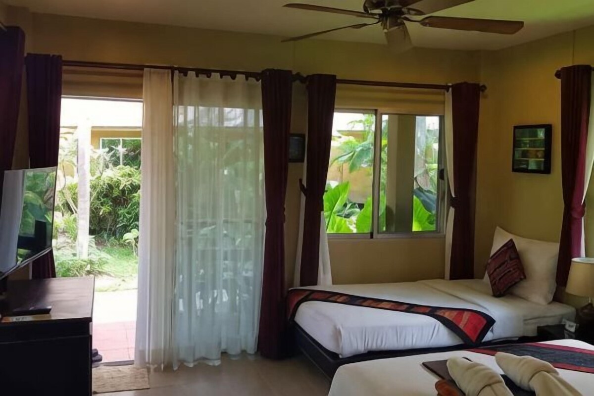 Una habitación de hotel con una cama, televisión, ventilador de techo y ventana con cortinas.