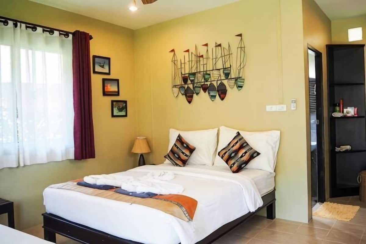 A bedroom with a bed, pillows, a nightstand, a lamp, a wall art piece, and a door leading to another room.