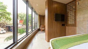 Habitación de hotel con un ventanal grande, una cama con cubrecama verde, un panel de pared de madera y un televisor de pantalla plana montado en la pared.
