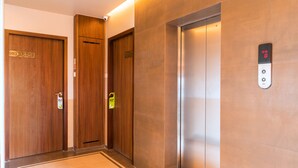 Un ascensor de hotel con pantalla digital, puertas de madera y suelo de baldosas.