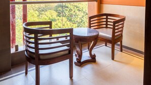 Un balcón con dos sillas de madera y una mesa pequeña, con vistas a un paisaje urbano con edificios y árboles.
