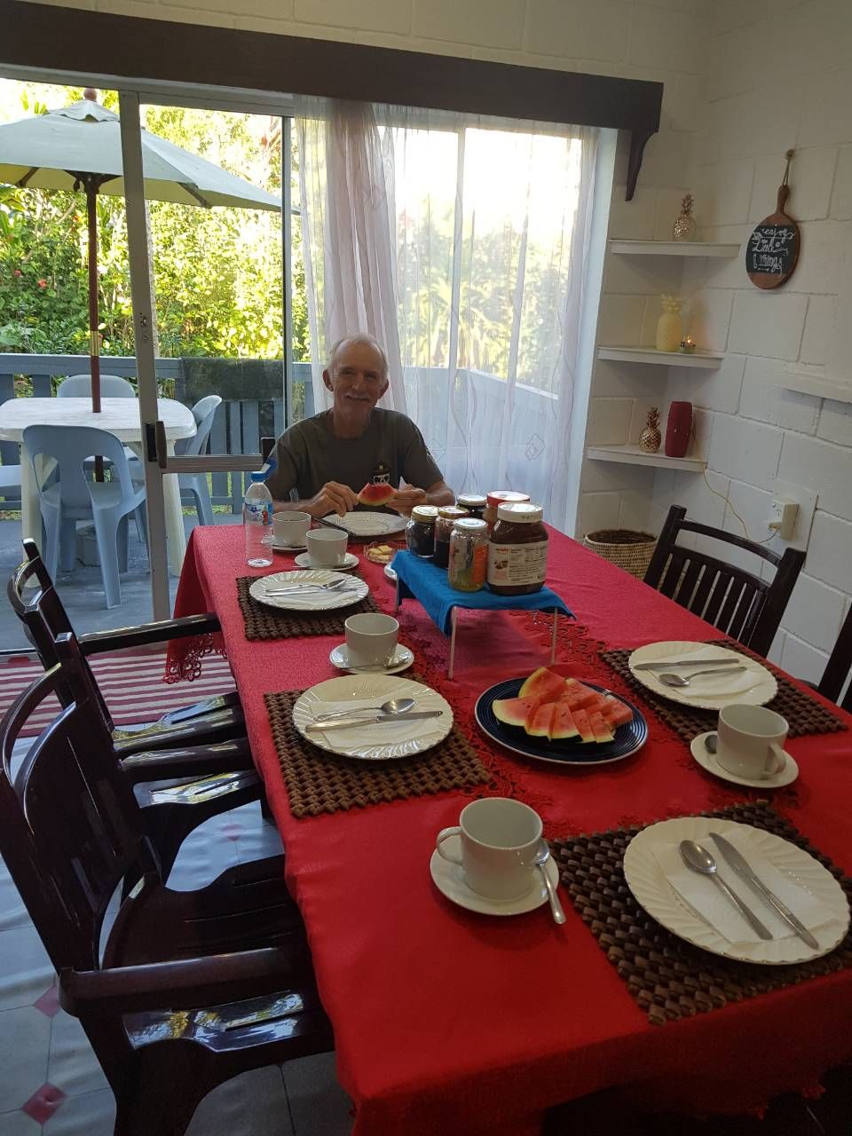 A dining table set with plates, cutlery, and condiments, with a view of greenery outside.