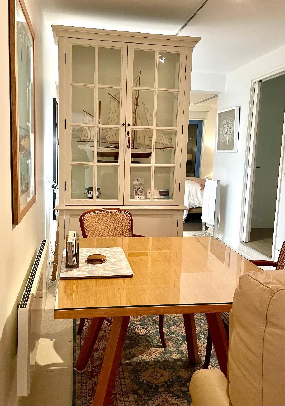 Un comedor con mesa de madera, sillas, una vitrina y un tapete estampado.
