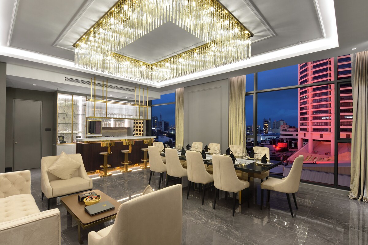 A modern dining area with a chandelier, a bar, and a view of the cityscape at night.