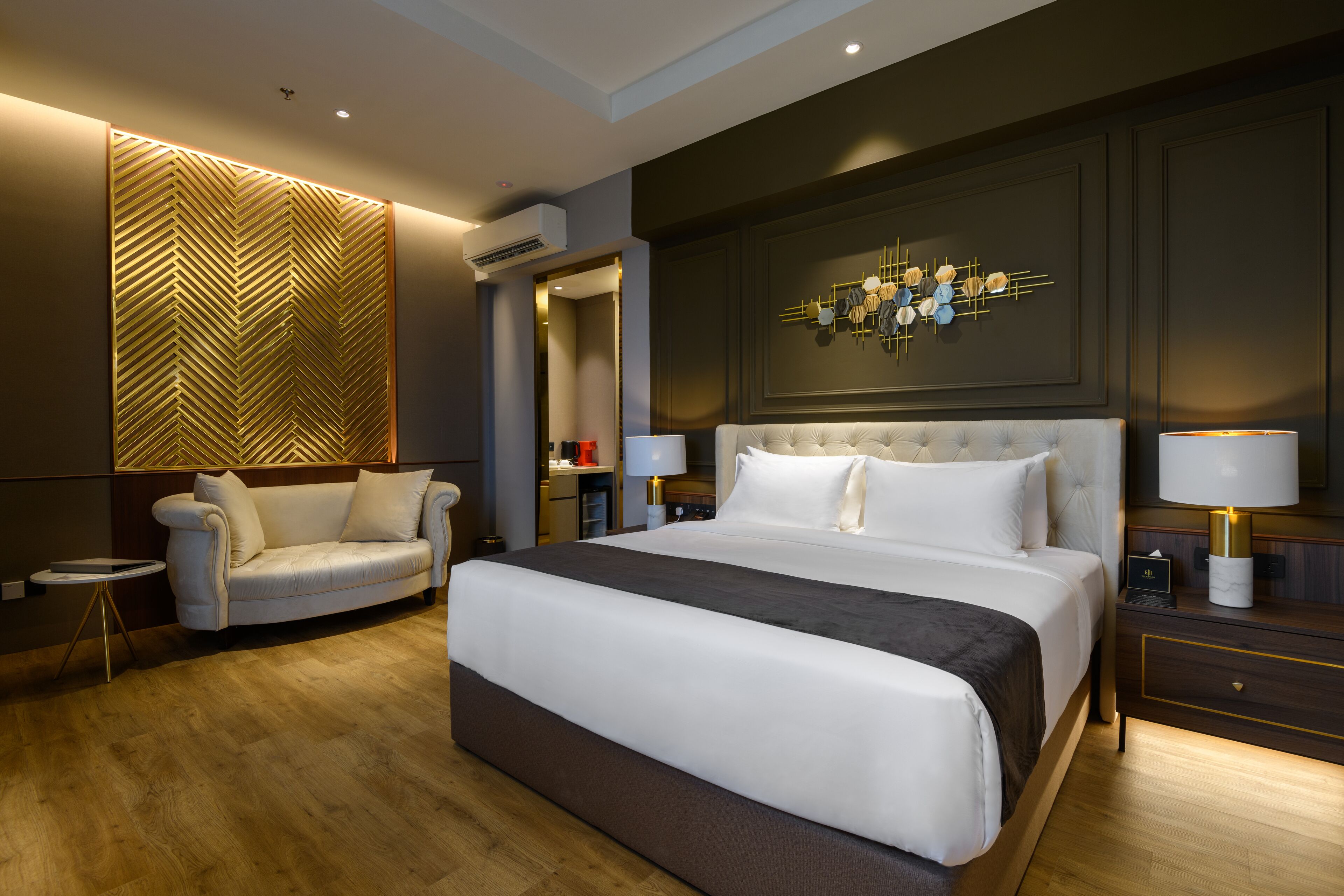 A modern hotel room with a large bed, a sofa, a side table, and a decorative wall panel.