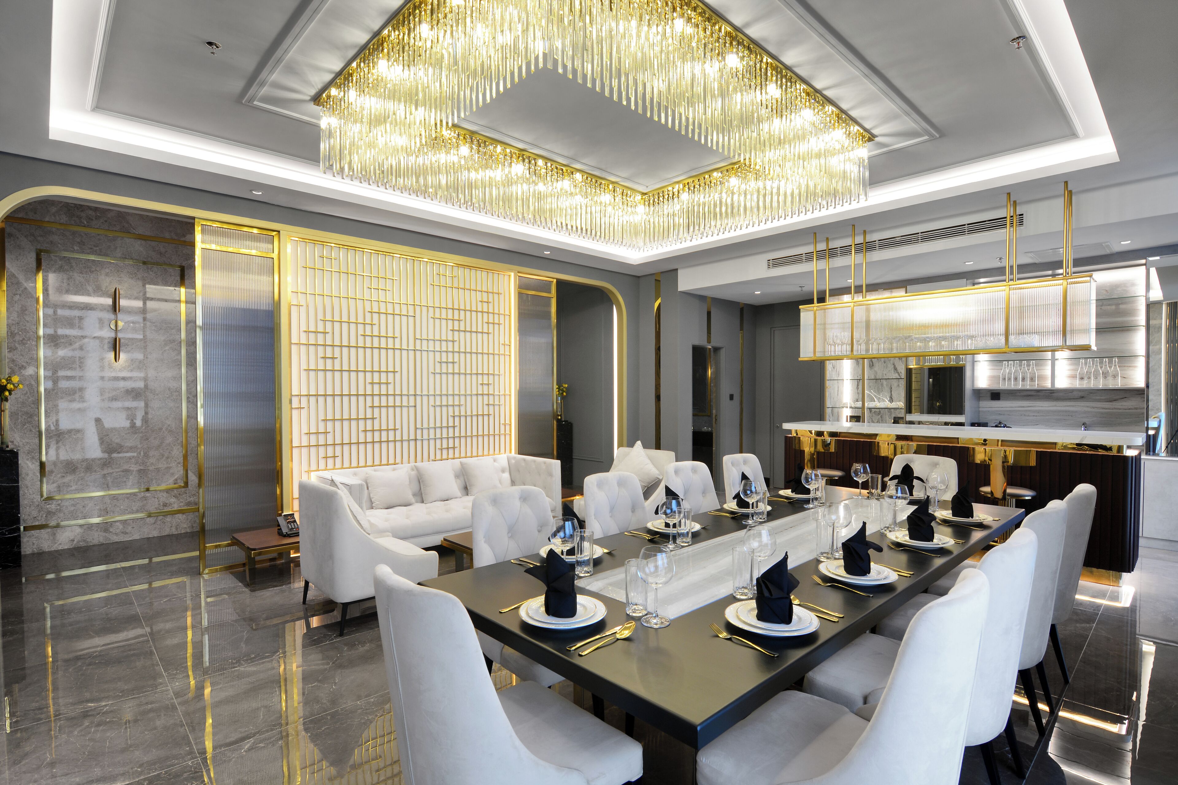 A modern dining room with a long table set for a meal, white upholstered chairs, and a chandelier.