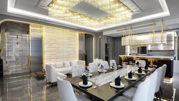 A modern dining room with a long table set for a meal, white upholstered chairs, and a chandelier.