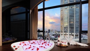 A bathroom with a bathtub filled with rose petals, a towel, and a tray of toiletries. - The Granite Luxury Hotel Penang (George Town)