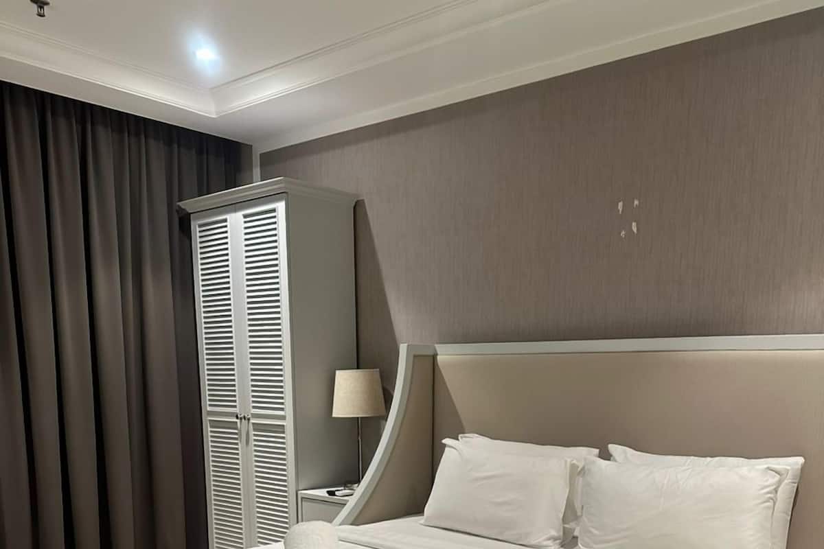 A hotel room with a large bed, a nightstand, a lamp, and a wardrobe.