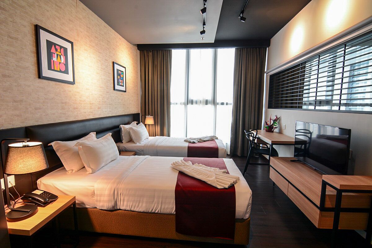 Una habitación de hotel con dos camas, un escritorio, un televisor y una ventana con cortinas.