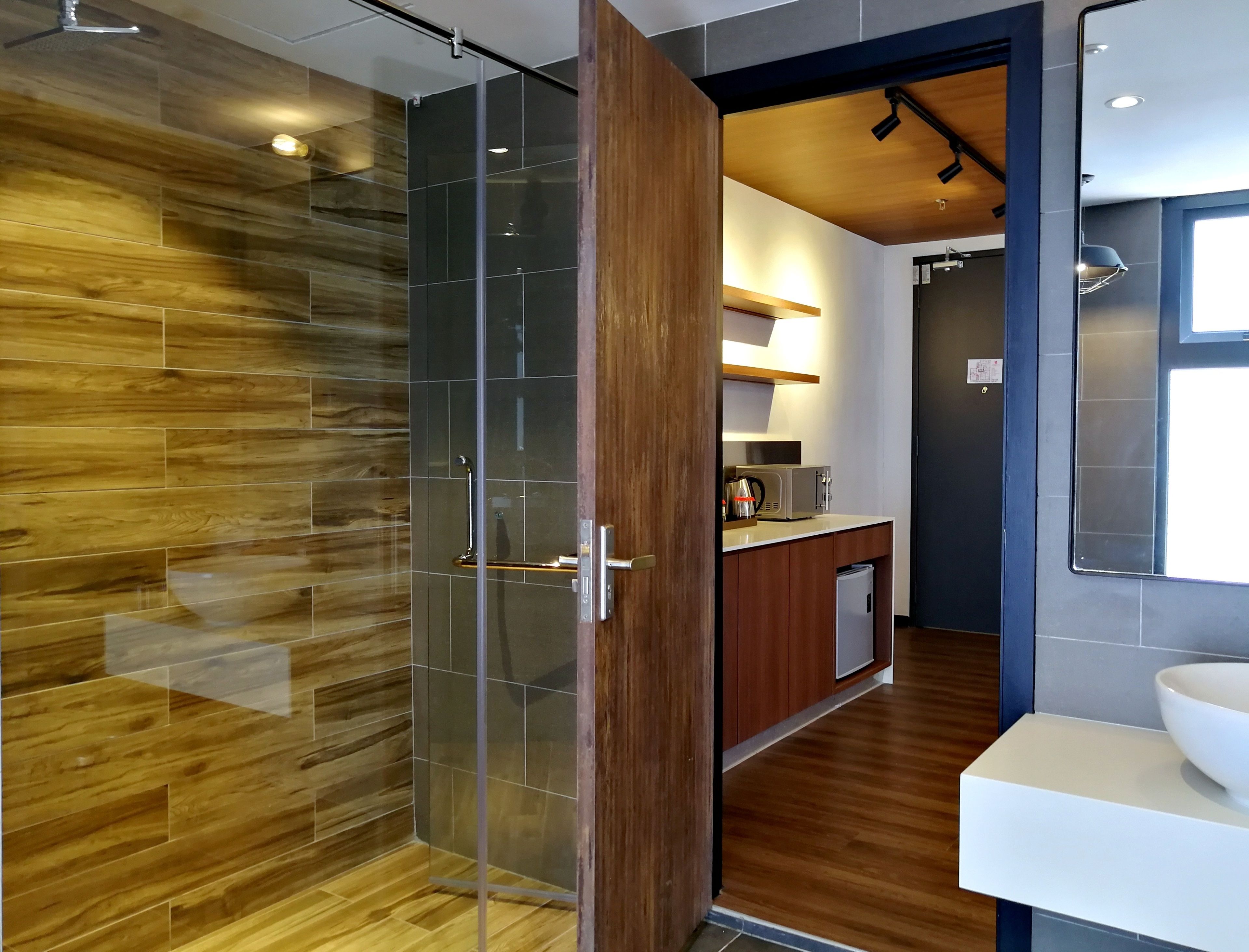 A modern bathroom with a glass shower enclosure, wooden flooring, and a white sink.