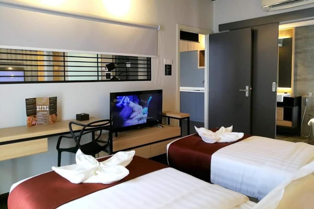 A hotel room with two beds, a desk with a television, a minibar, and a bathroom with a shower.