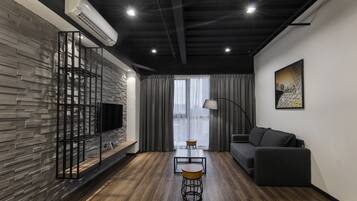 A modern living room with a stone wall, a black sofa, a TV, and a dining table with stools.