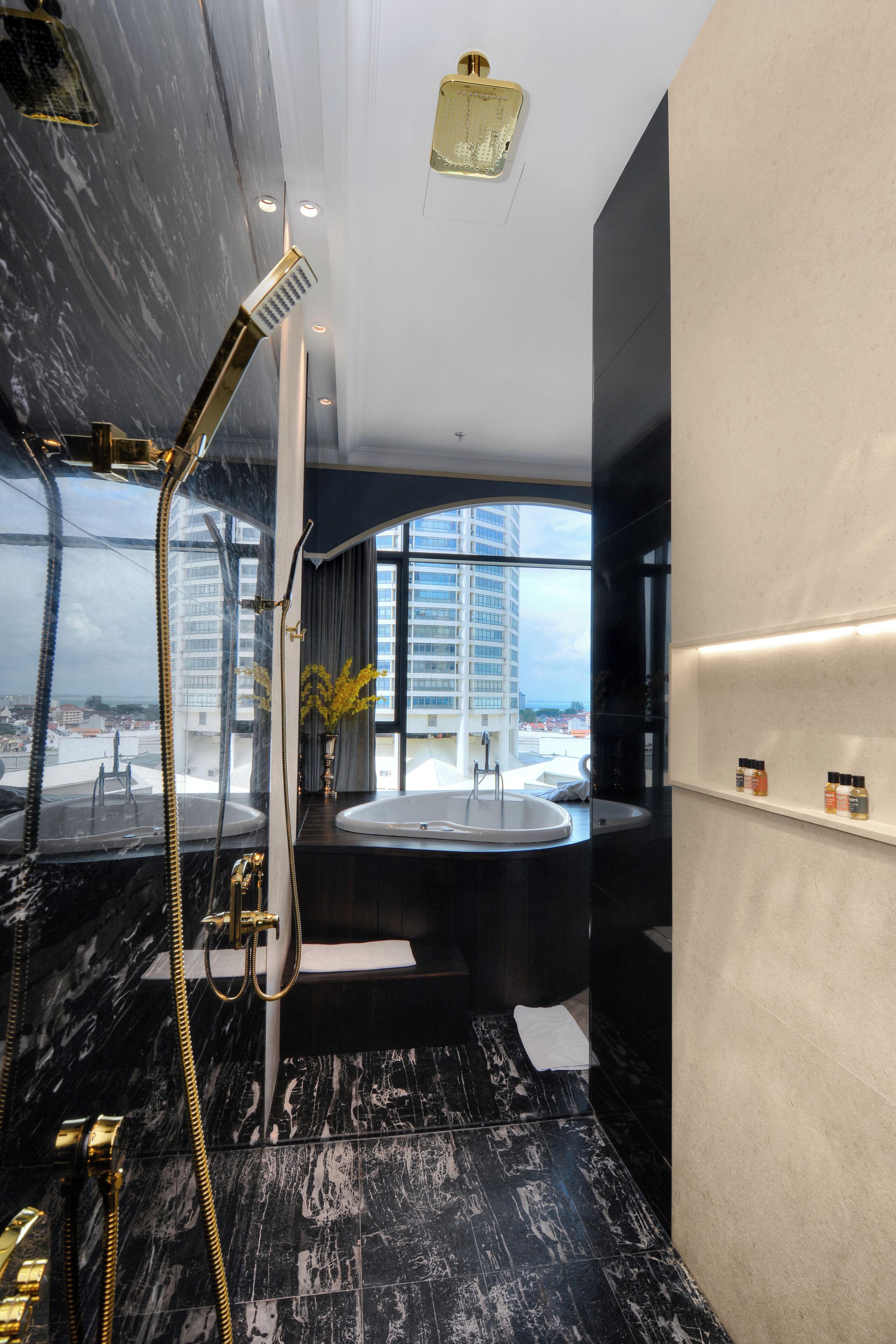 A modern bathroom with a large window, a bathtub, and a shower with a gold hose.