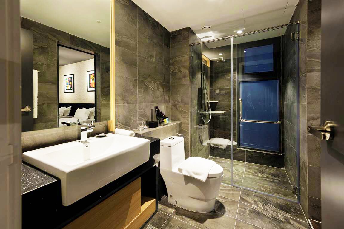 A modern bathroom with a large mirror, a white sink, a toilet, and a glass-enclosed shower area.