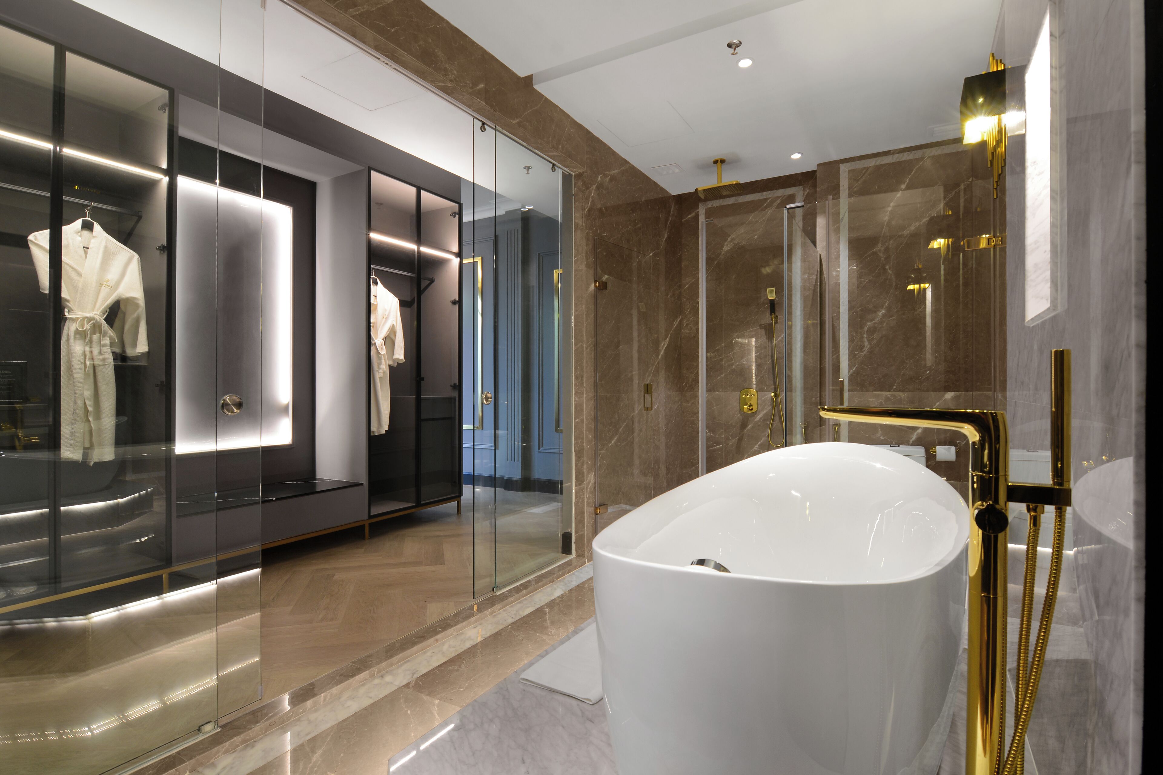 A modern bathroom with a large white bathtub, glass-enclosed walk-in closet, and marble walls.