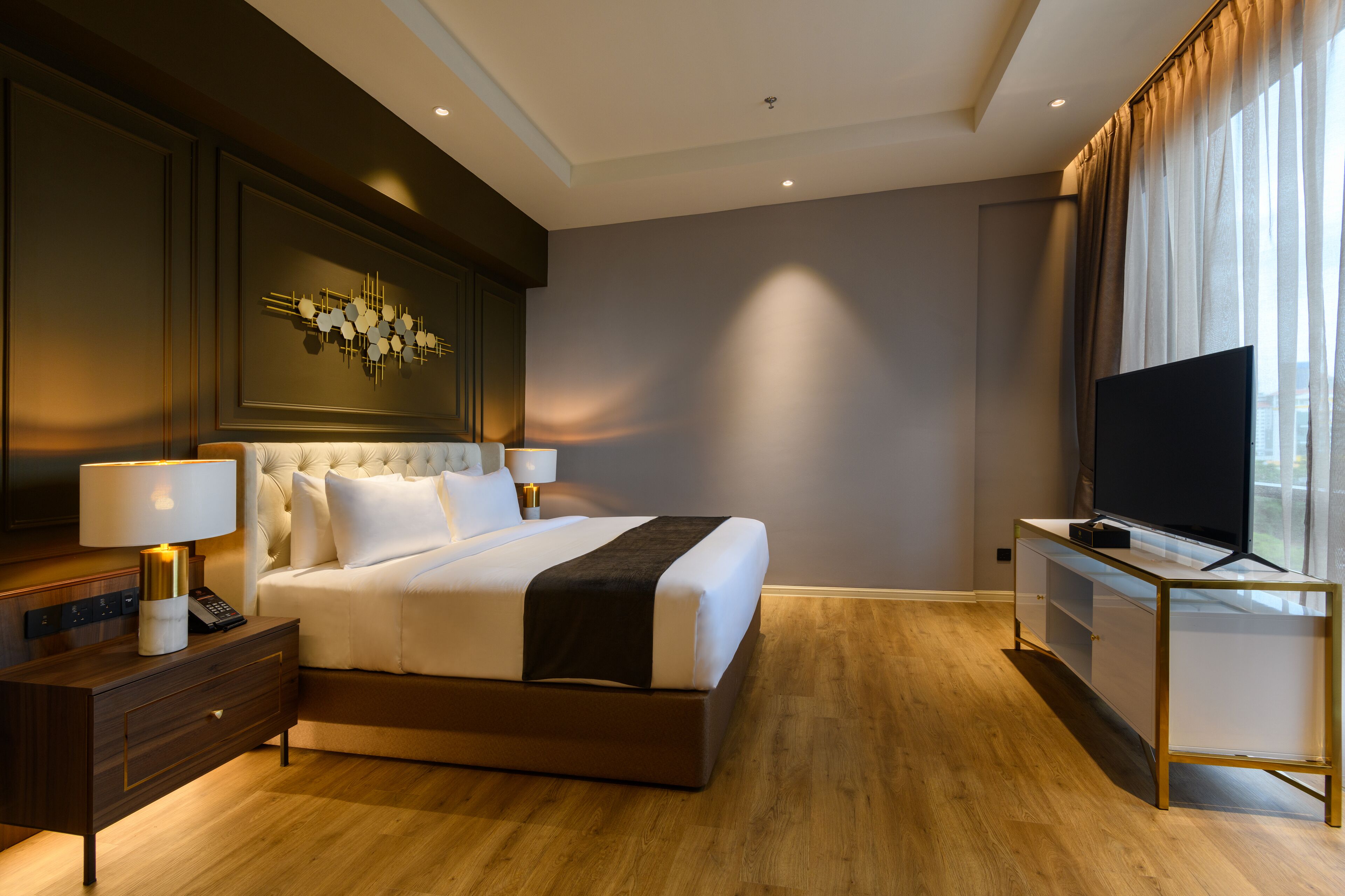 A modern hotel room with a large bed, a flat-screen TV, a bedside table with a lamp, and a decorative wall piece.