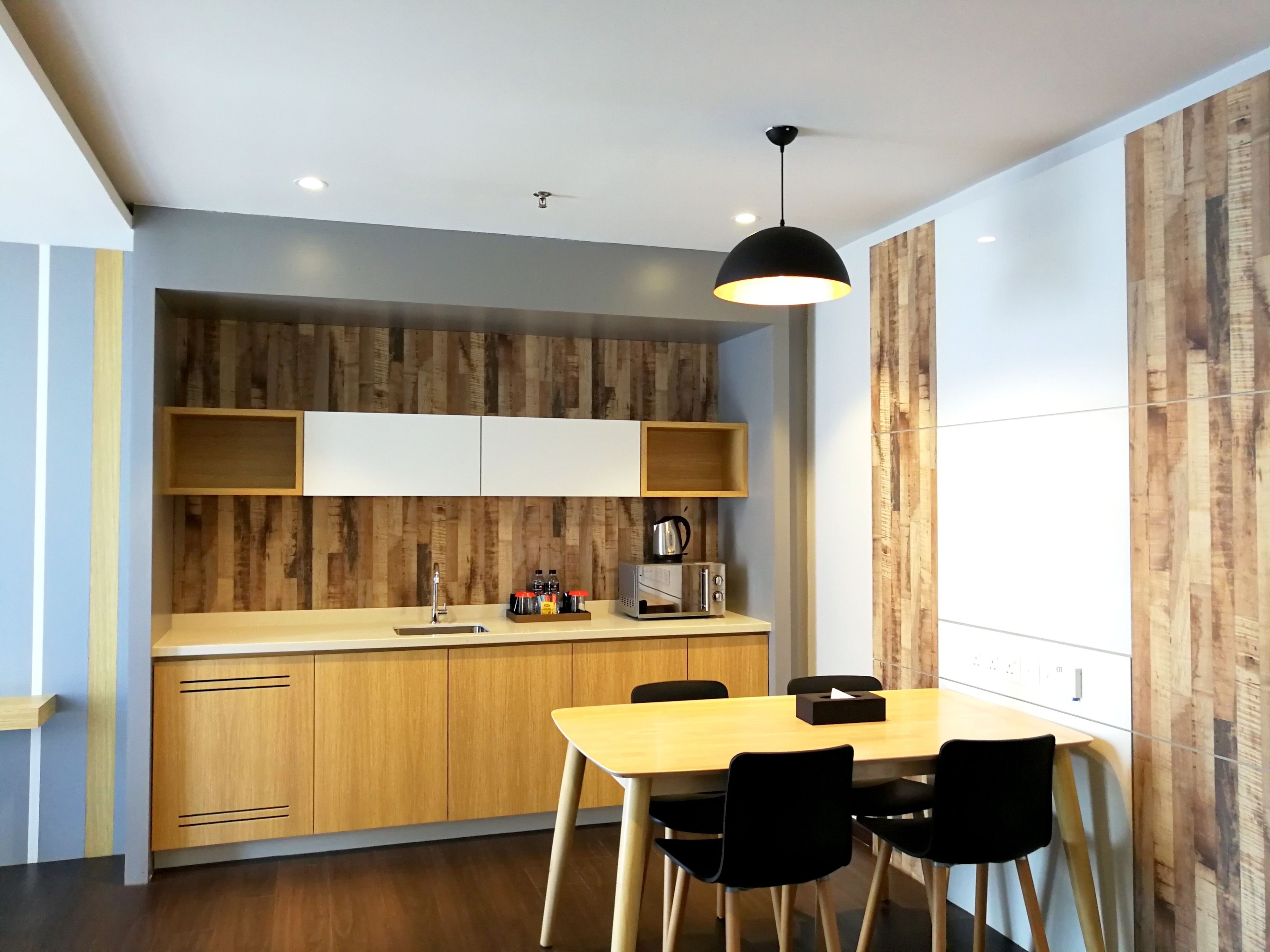 A modern kitchen with wooden cabinets, a wooden countertop, a sink, a kettle, a toaster, and a dining table with chairs.