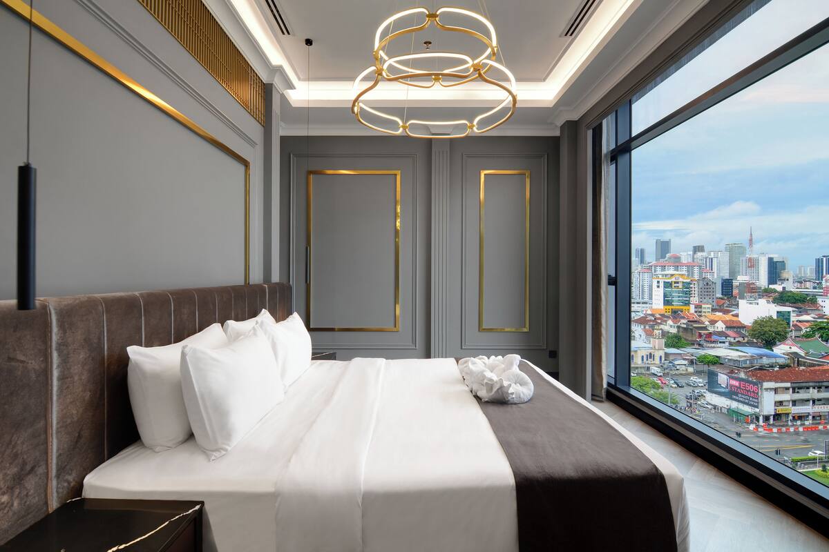 A modern hotel room with a large bed, a view of the city, and a unique ceiling light fixture.