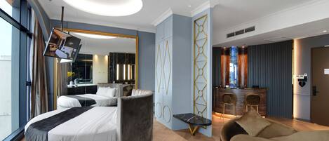 A modern hotel room with a curved bed, a sofa, a dining area with a bar, and a large mirror.