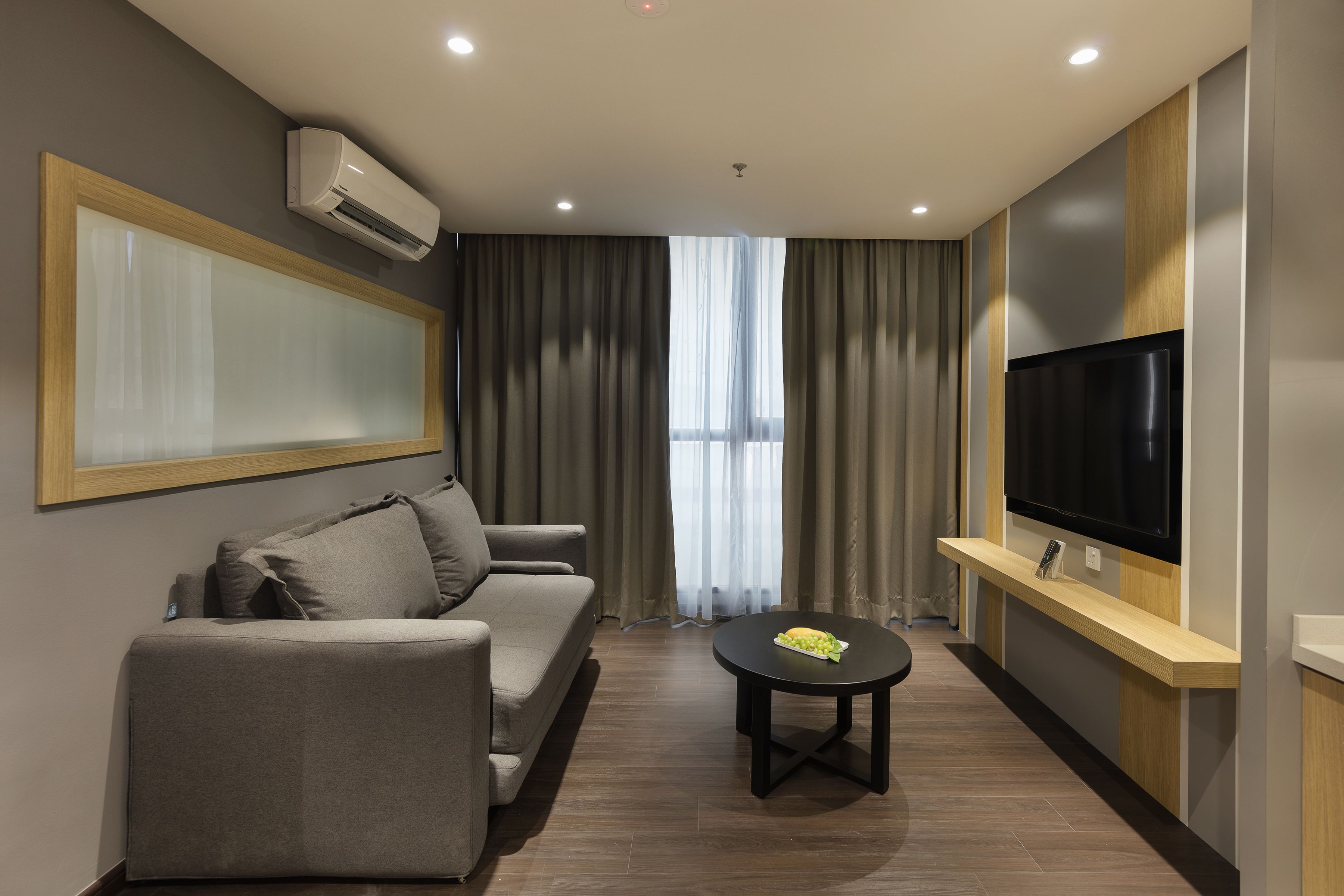 A modern living room with a sofa, a coffee table, a TV, and a large window with curtains.
