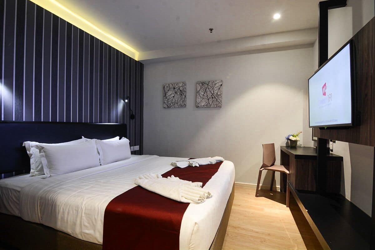 A modern hotel room with a large bed, a flat-screen TV, and a wooden desk.