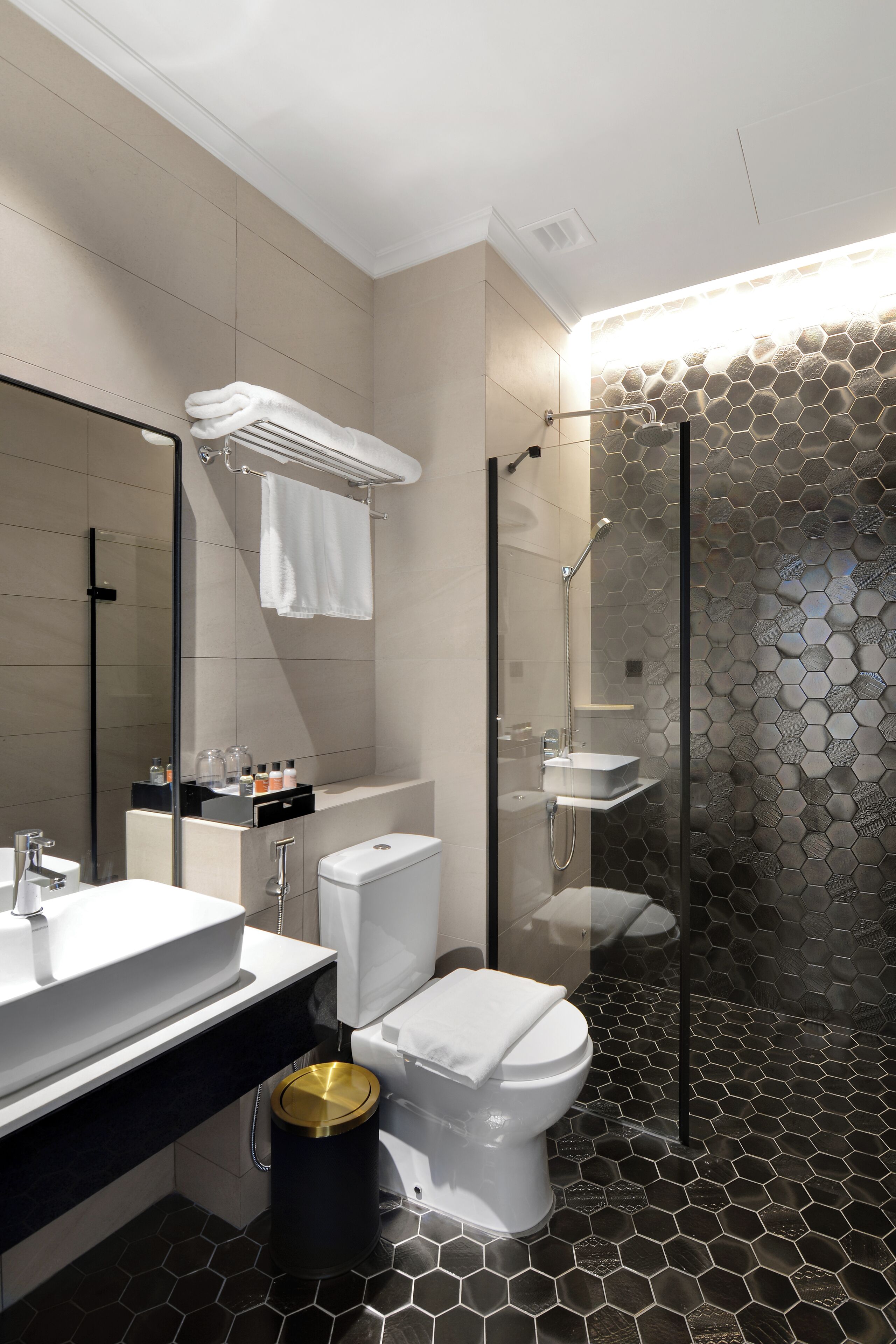 Un baño moderno con ducha de vidrio, inodoro blanco y cubo de basura negro.