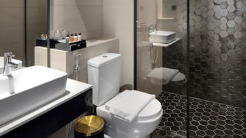 Un baño moderno con ducha de vidrio, inodoro blanco y cubo de basura negro.