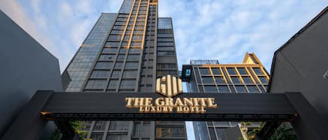 The Granite Luxury Hotel with a prominent entrance sign, tall buildings in the background, and a clear sky.