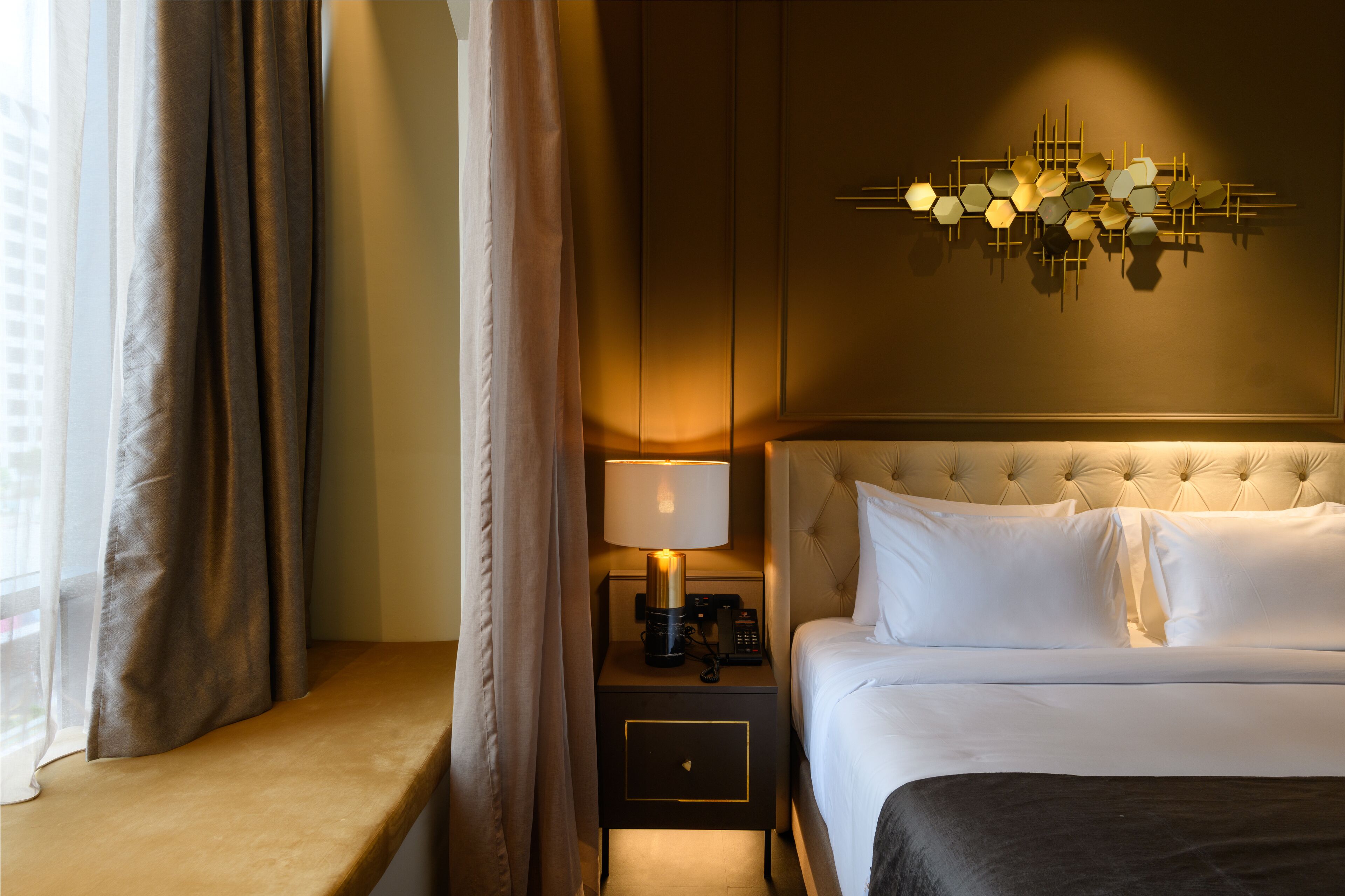 Habitación de hotel con cama, mesita de noche con lámpara, aplique de pared y ventana con cortinas.