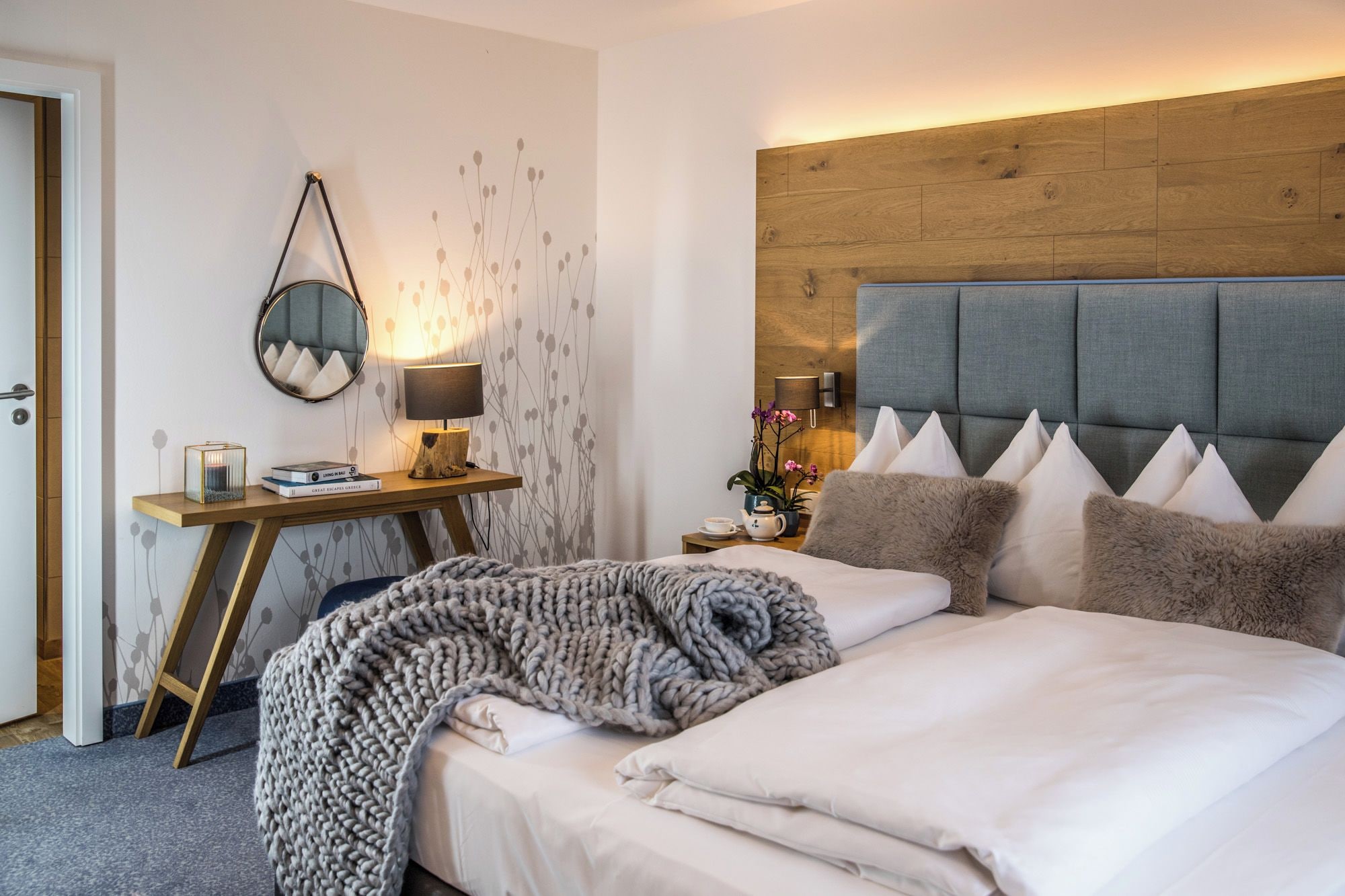 A hotel room with a bed, bedside table, lamp, and a wall-mounted mirror.