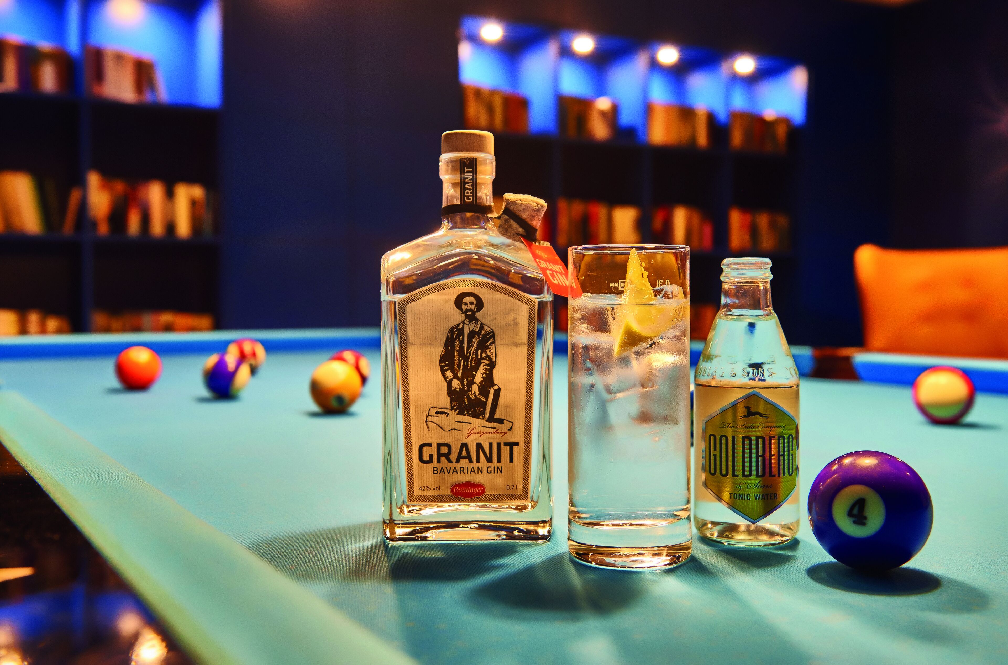 A billiards table with three bottles of liquor and a pool cue.