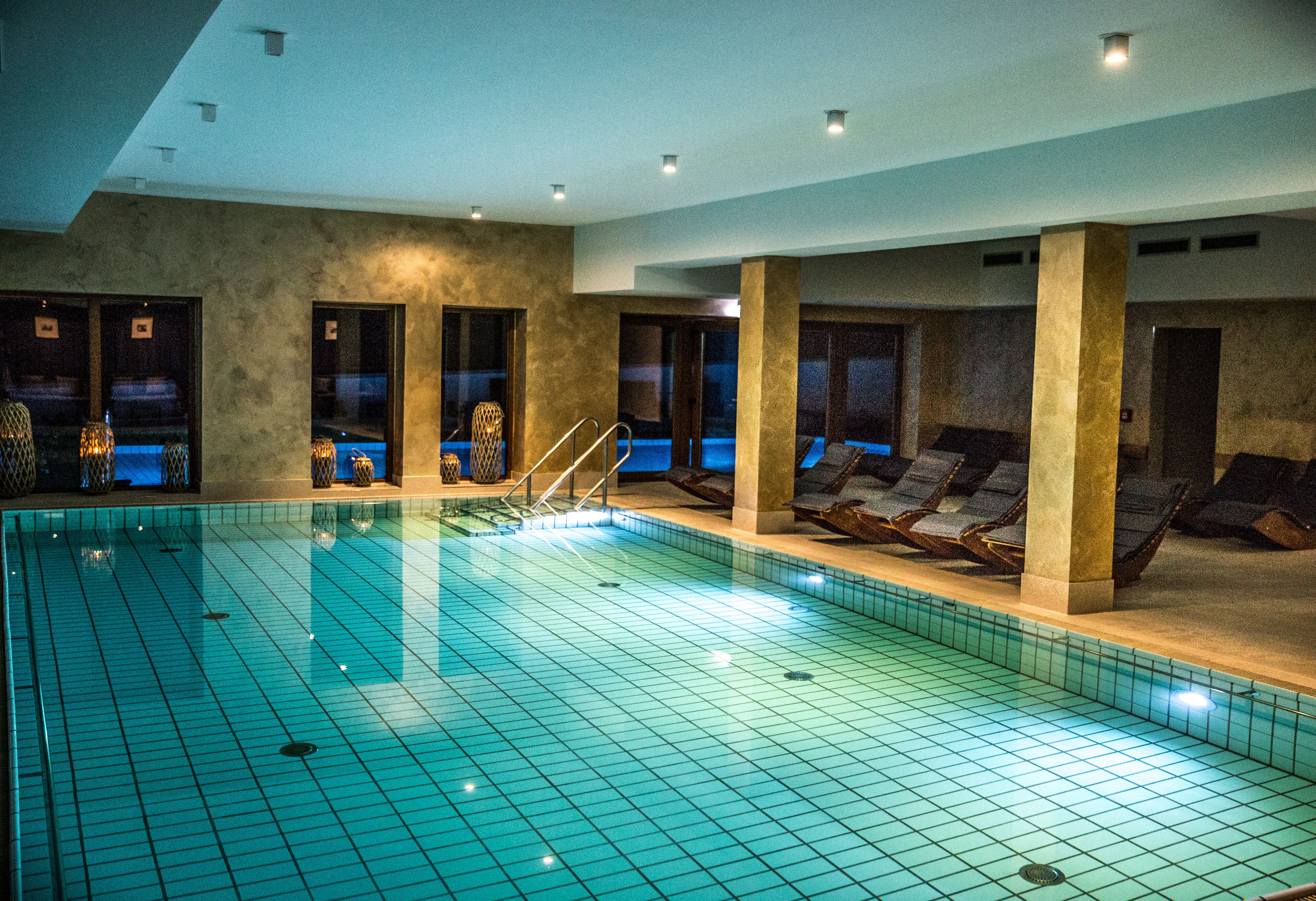 An indoor swimming pool with tiled walls, lounge chairs, and a staircase leading to a higher level.